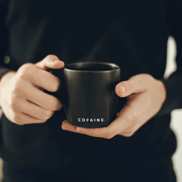 Taza de café Cofaine sostenida entre las manos
